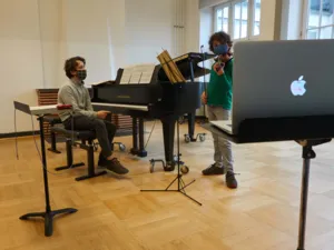 Zwei Jungs an Klavier und Geige. Sie schauen auf einen Laptop.